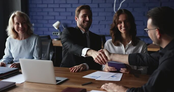 Group of millennial businesspeople take part in meeting, leaders shake hands thanking for successful negotiations, cooperation, finish meeting express respect. Make commercial deal, business etiquette