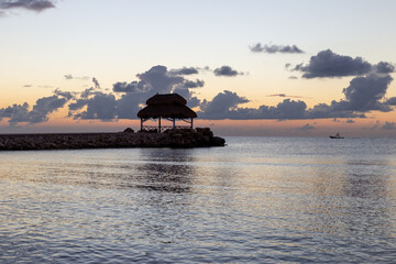 silhouette d'une cabane avec un toit de paille sur la mer lors d'un lever de soleil doux