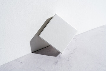 One small white square gift box mockup on gray concrete background. Closeup, shadows, minimalist concept