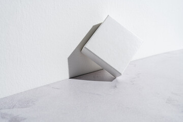 One small white square gift box mockup on gray concrete background. Closeup, shadows, minimalist concept