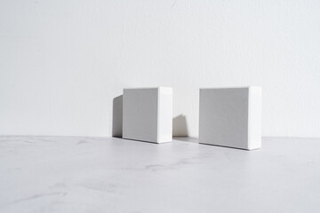 Two white square gift boxes mockup on gray concrete background. Closeup, shadows, minimalist concept