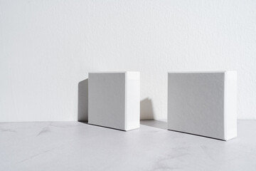 Two white square gift boxes mockup on gray concrete background. Closeup, shadows, minimalist concept - 547599314