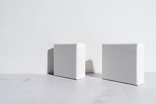 Two white square gift boxes mockup on gray concrete background. Closeup, shadows, minimalist concept