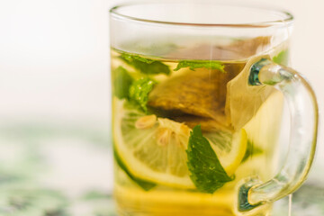 Close up shot of a transparent cup with brewing tea bag in it, lemon and mint. Refreshment