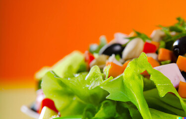 Vegetable Salad Closeup with orange background. Healthy organic salad with lettuce, tomatoes, onion, olives and cucumbers