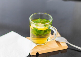 Close up shot of a transparent cup with brewing tea bag in it, lemon and mint. Refreshment