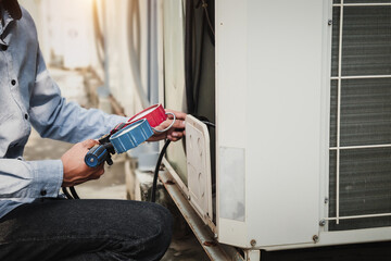 Mechanic  air conditioner technician is using a manifold gauge to check the refrigerant in the system to inspect and repair the outdoor air compressor.