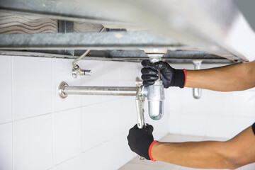 Technician plumber using a wrench to repair a water pipe under the sink. Concept of maintenance,...