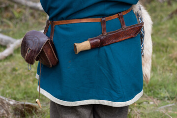 Back view of a viking man in blue wool tunic with sax knife in a  leather sheath and a small leather  bag on the belt.