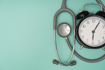 Top view of stethoscope and alarm clock on the green background, schedule to check up healthy concept