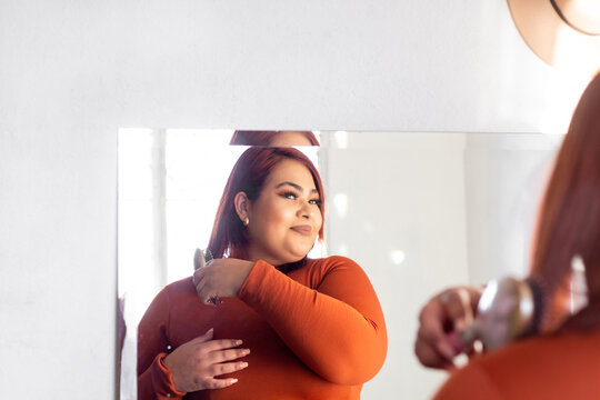 Fat Hispanic Young Woman In Front Of Mirror Combing Her Hair. Plus Size Latina Model