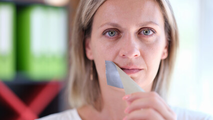 Woman removes adhesive tape covering her mouth.