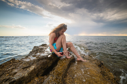 A young, beautiful woman relaxes with wine on a rock in the water of the Adriatic Sea in Croatia