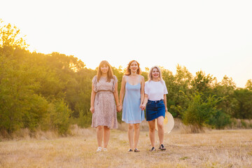 Fototapeta premium A group of girlfriends jumps and runs outdoors. A group of female friends hugs and enjoys the sunset in nature. Laughter, smiles and joy.