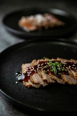 Closeup of steak tataki in soy caramel sauce served on black plate with blurry background