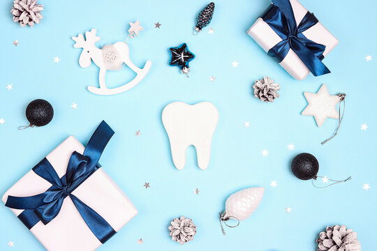 White tooth surrounded by Christmas decorations and gifts on blue background.