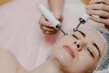 Obraz na płótnie Canvas A young European woman, a brunette, is undergoing a microcurrent galvanic face lift with the help of electrodes. The concept of preventing the problem of acne and oily skin.
