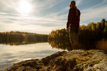 Male hiker standing on the shore of a forest lake taking in the view a beautiful sunny fall morning