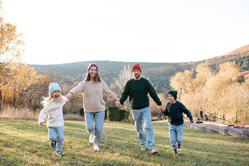 Happy family running in rustic scene with green grass and autumn nature background together holding hands. Cheerful and happiness.