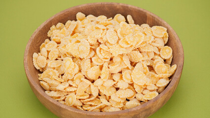 Corn flakes in a wooden bowl, green background. Breakfast concept