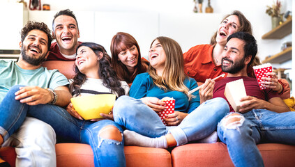 Obraz premium Young friends having genuine fun together at home watching movie on smart tv - Cozy life style concept with happy people relaxing on sofa couch eating popcorn and takeaway food - Bright vivid filter