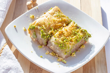 Traditional East Asian sweet baked bahlava or pahlava with nuts and syrup on a white plate on light wooden background.