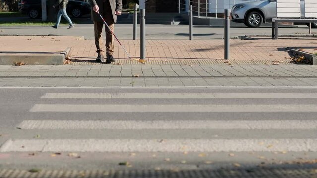 Visually impaired man crossing the road with his stick with the help of tactile pedestrian sidewalk for the visually impaired in the city.