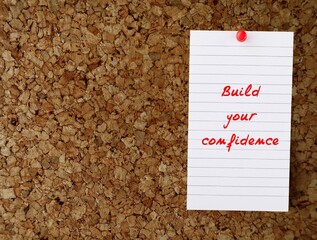 Cork board with handwritten text note BUILD YOUR CONFIDENCE - to boost feeling of self-assurance,...