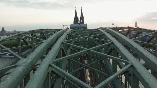 Drone is flying in slow-motion along the Hohenzoller Bridge in Cologne, there are two trains on the bridge,  the drone is flying straight towards the Cologne Cathedral