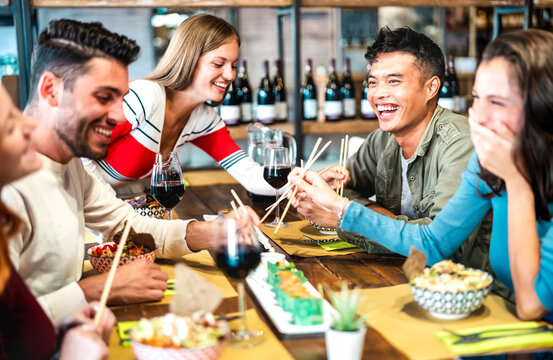 Multicultural trendy friends eating sushi with chopsticks at fusion restaurant bar - Food and beverage life style concept with happy young people having fun together at cool eatery - Vivid filter