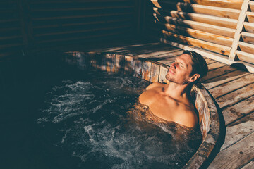 Man relaxing in wooden hot tub outdoor. 