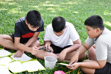 Three Asian studets holding magnifying glasses and other learning devices, tablets, small fishing...