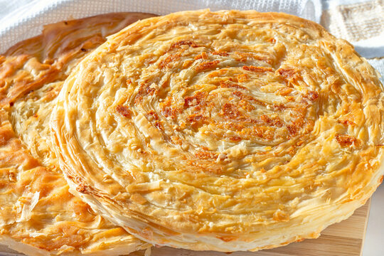 Traditional homemade Tajik Fatir (layered flat bread) with cheese and onion on light wooden background close up.