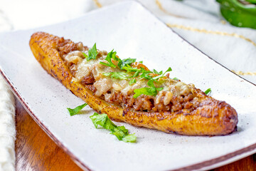 Baked Sweet Ripe Plantain Canoe (Canoas de Platanos Maduros) stuffed with ground meat, cheese and greens on a plate on wooden background.