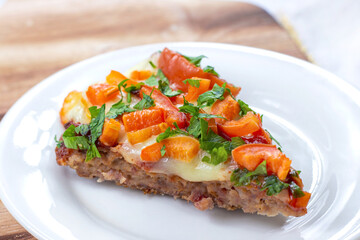 Tasty homemade Low-Carb Keto Meatza (grain and gluten free beef meat-based pizza) slice with vegetables and mozzarella cheese on a white plate on wooden background close up.