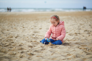 Adorable toddler girl playing on the sand beach in North Holland, the Netherlands