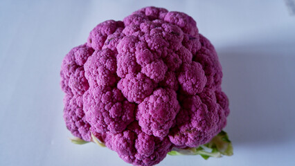 Whole violet cauliflower on the white floor, isolated, side view.