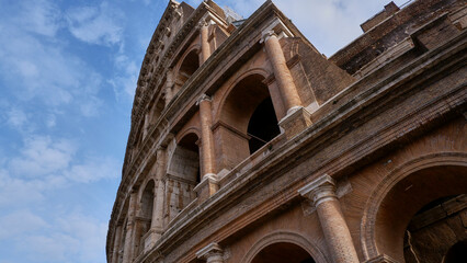 Colesseum on the white cloudy and blue sky background, from below or on the edge.