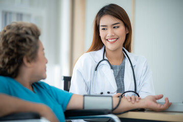Fototapeta premium Smiling young female doctor checking and measuring blood pressure of senior patient