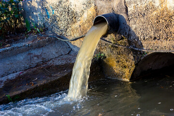 Wastewater sewage pipe dumps the dirty contaminated water into the river. Water pollution,...