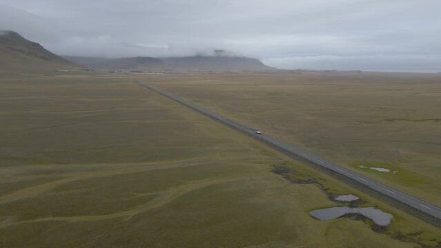 Aerial descending Cars Driving Along an Asphalt Road along Green Meadows and foggy mountains, Iceland