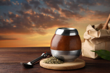 Calabash with mate tea and bombilla on wooden table outdoors at sunset. Space for text