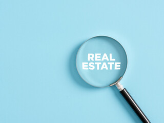 Magnifier with the text real estate on blue background. Real estate search