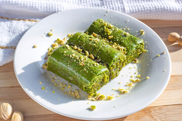 Traditional East Asian sweet baked pistachio baklava or pahlava with nuts and syrup on a white plate on light wooden background.