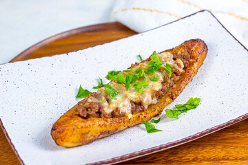 Baked Sweet Ripe Plantain Canoe (Canoas de Platanos Maduros) stuffed with ground meat, cheese and greens on a plate on wooden background. - 547643141
