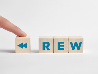 Finger presses the rewind REW button on wooden cubes.