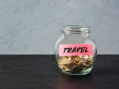 Glass jar with coins and the word travel on a label. Saving money for holiday travel and budget for vacation.