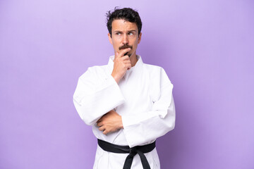 Young caucasian man doing karate isolated on purple background having doubts and thinking