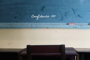 Green vintage school  chalkboard background , with handwritten chalk text CONFIDENCE 101 - with student old wood desk and chair as foreground.