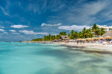 Naklejka premium People swimming near white sand beach with umbrellas, bungalow bar and cocos palms, turquoise caribbean sea, Isla Mujeres island, Caribbean Sea, Cancun, Yucatan, Mexico